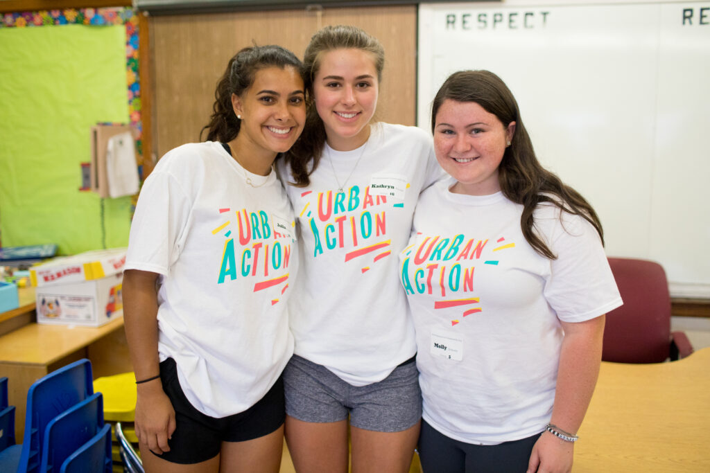 Three students volunteering in a school with colorful Urban Action tee shirts